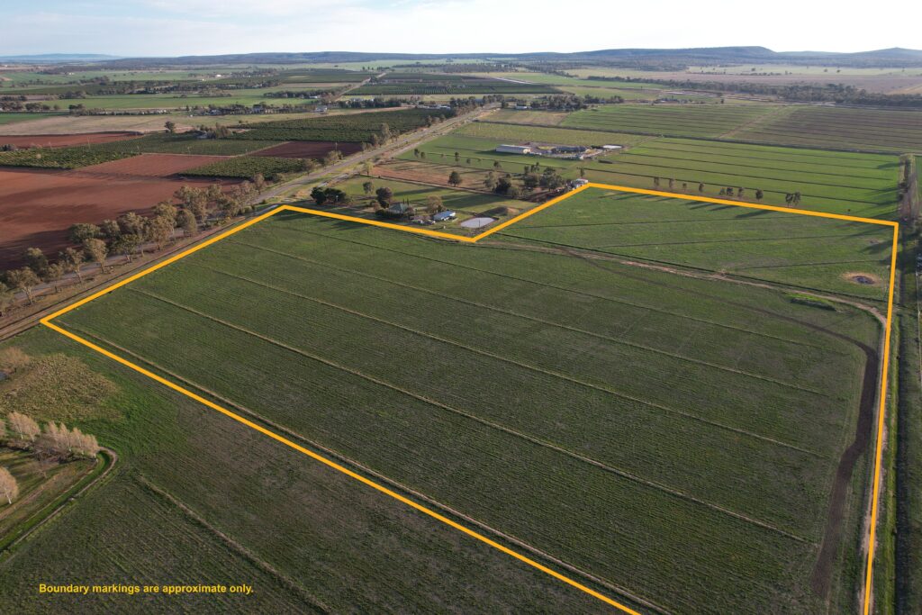 An aerial view of the development site, showing a large agricultural field bordered by yellow lines that indicate approximate boundary markings.
