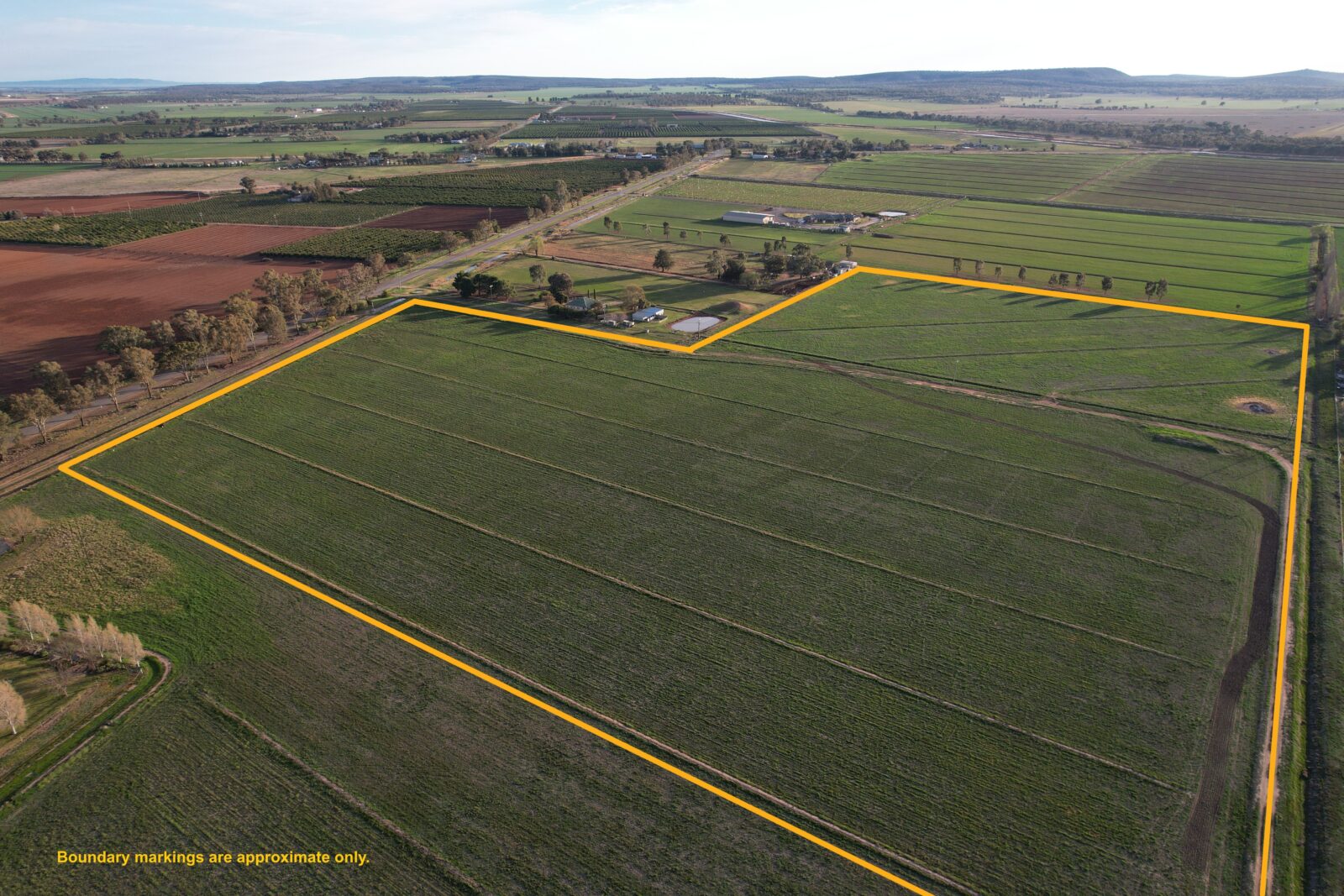 An aerial view of the development site, showing a large agricultural field bordered by yellow lines that indicate approximate boundary markings.