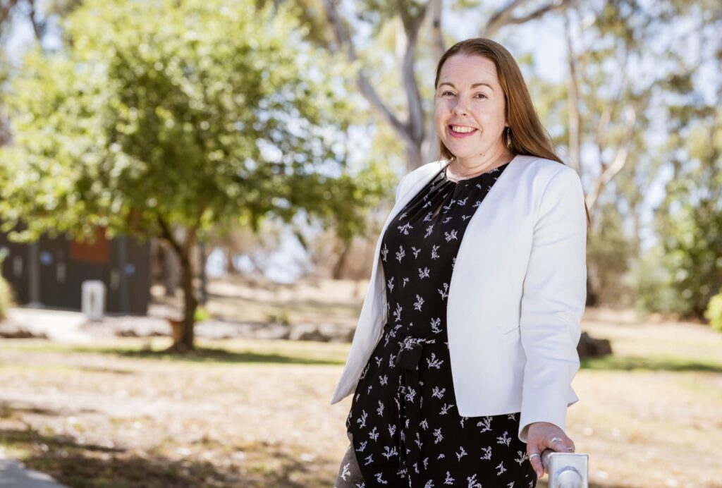 AgriFutures Managing Director Brianna Casey AM. Brianna is smiling, has long brown hair, and is wearing a white jacket over a black dress with white spots.
